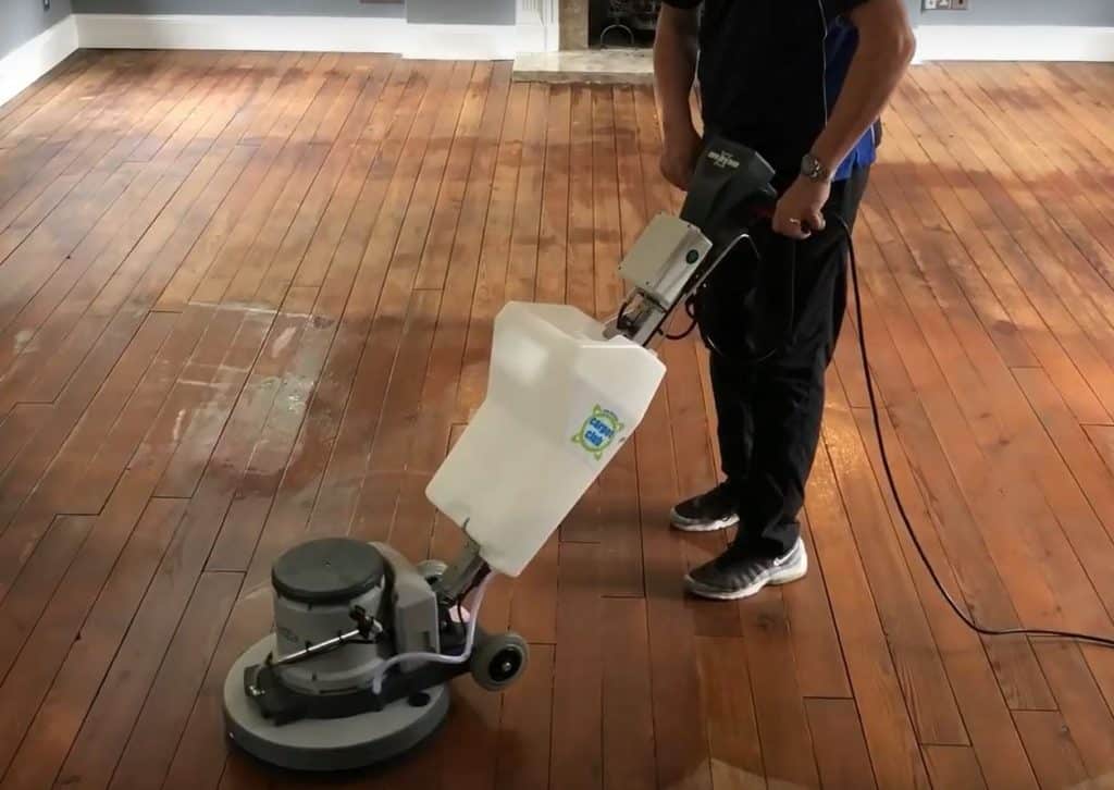 A man cleaning a wooden floor with a machine.