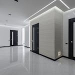 Modern spacious corridor with white walls and floor and black doors and ceiling decorated with LED lights