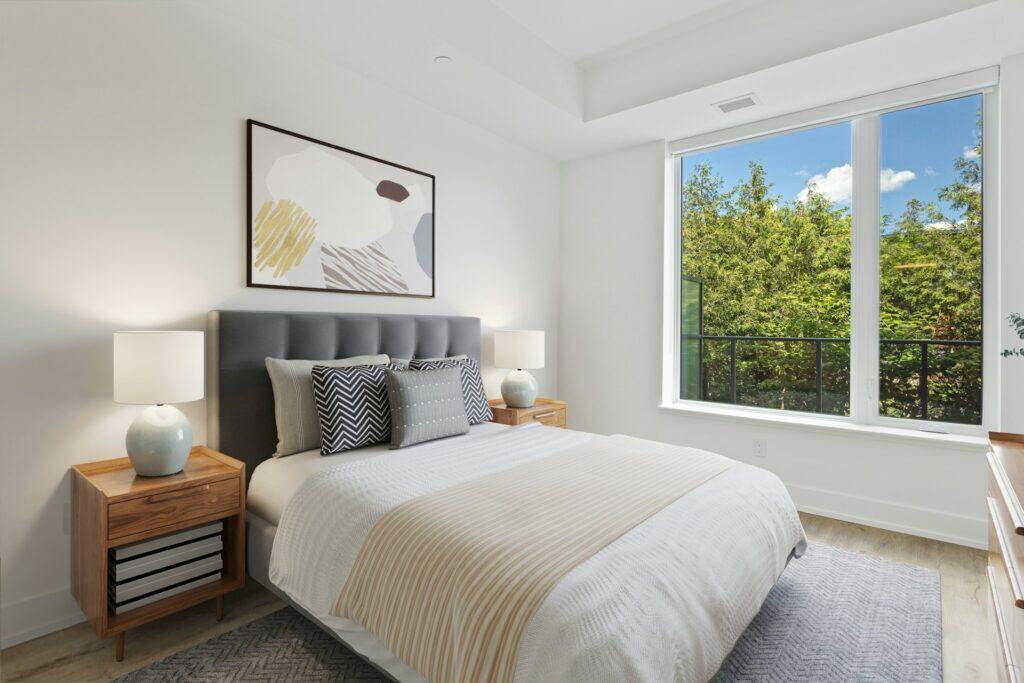 Zero Dry Time A modern bedroom with a neatly made bed, two wooden nightstands with lamps, abstract wall art, and a large window overlooking green trees.